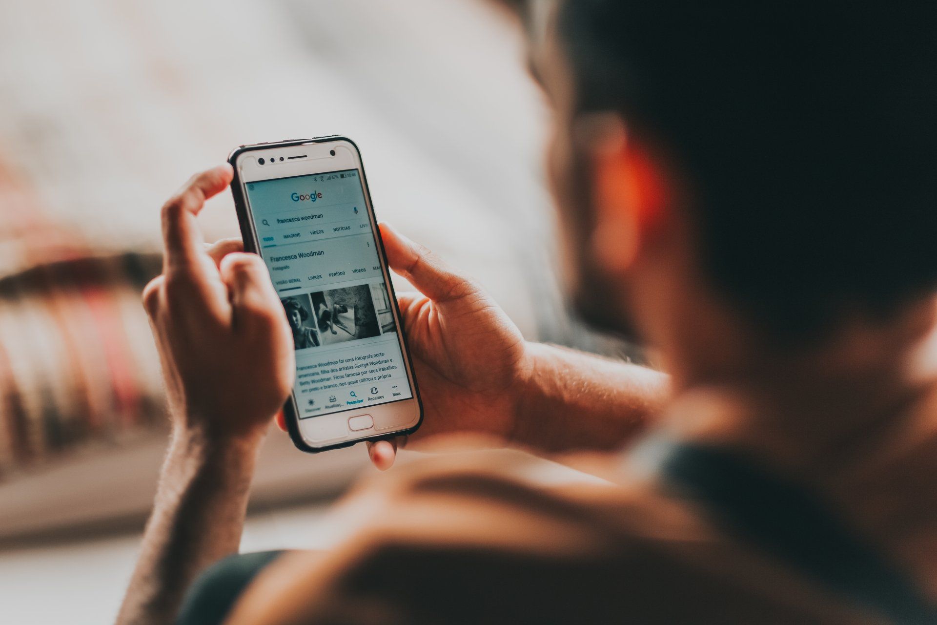 Person using a smartphone, browsing a webpage. White phone with black case held with both hands, soft focus background.