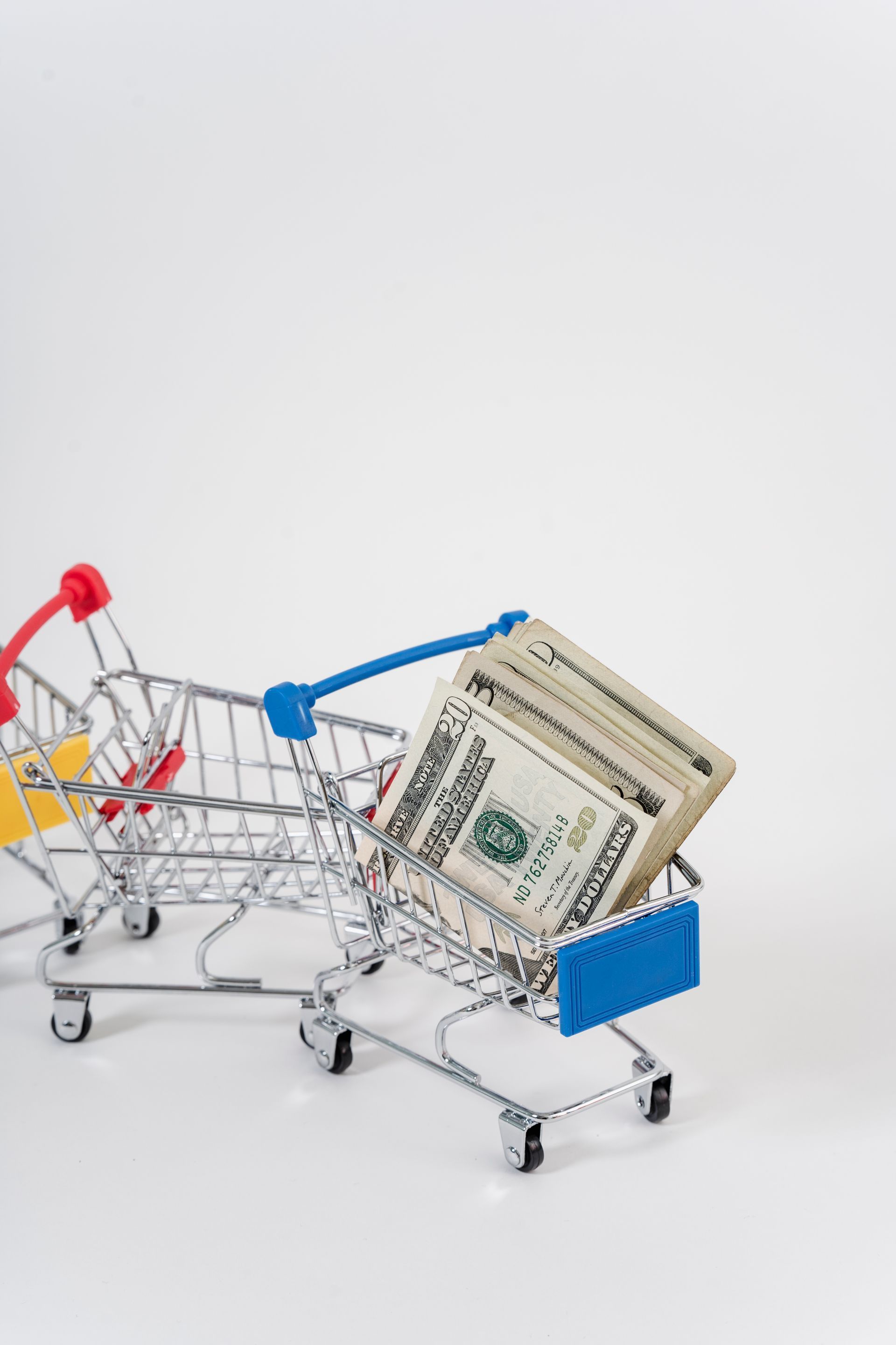 Miniature shopping cart filled with stacks of US dollar bills. Two empty carts are behind it.