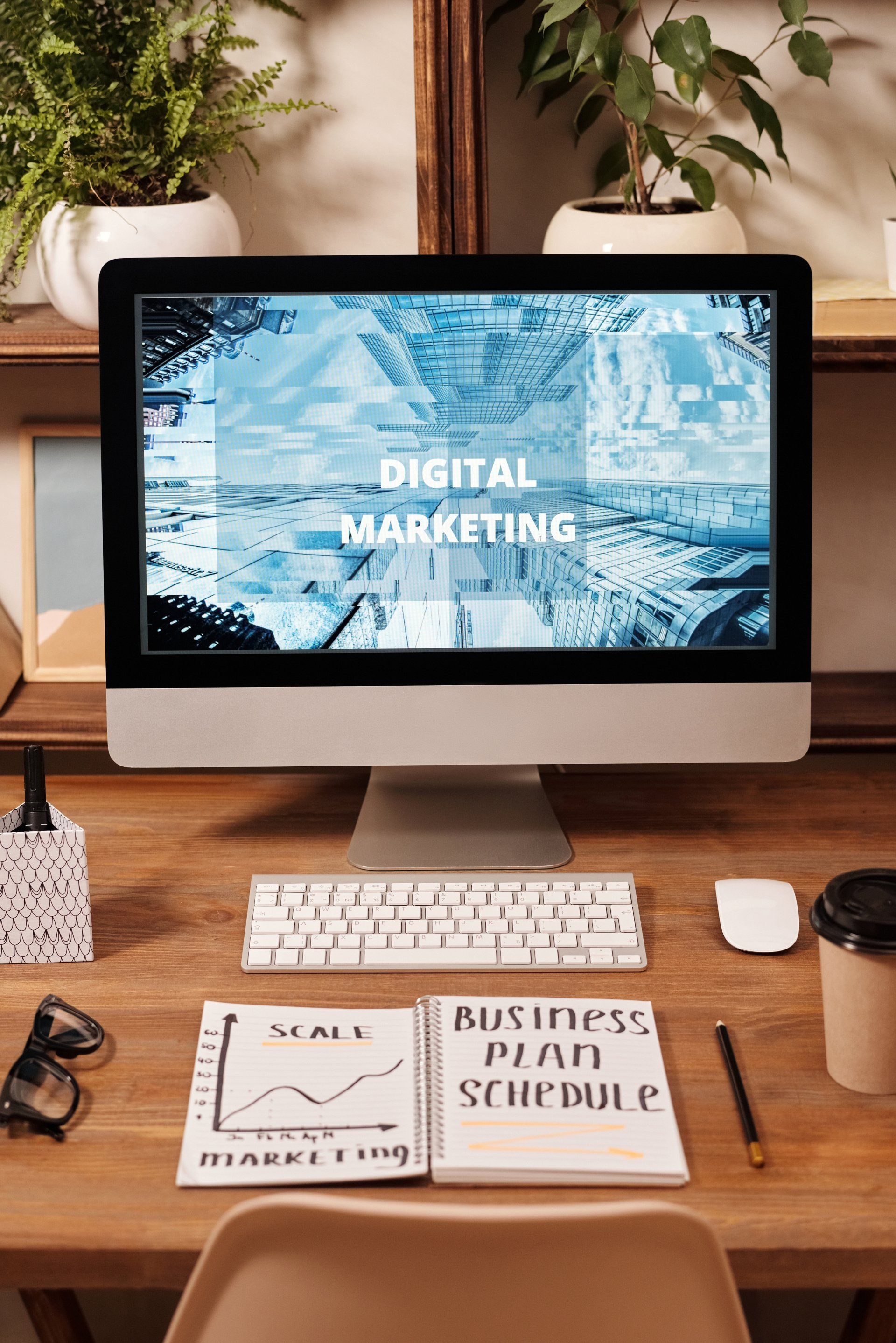Computer monitor displaying "Digital Marketing" on a desk with keyboard, notebook, and a cup.