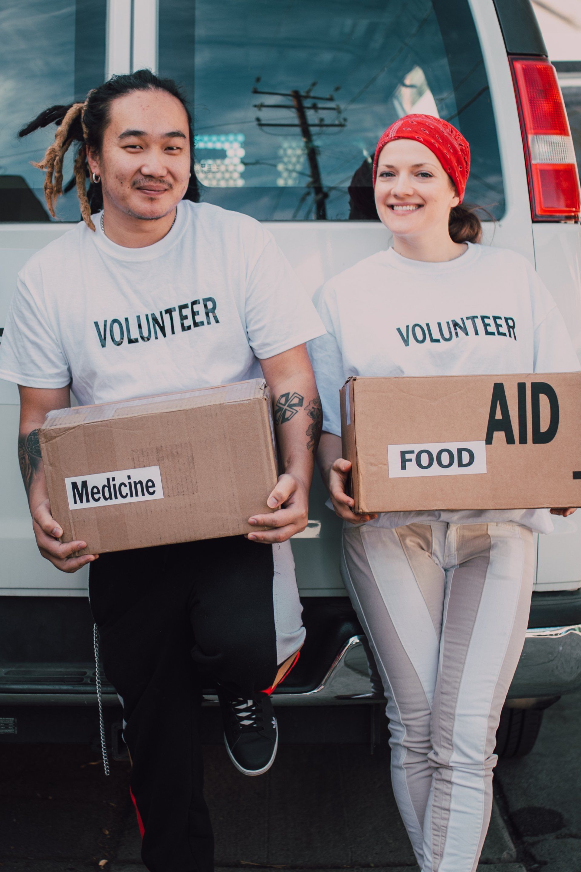Two volunteers with boxes of "Medicine" and "Food Aid" stand by a van.