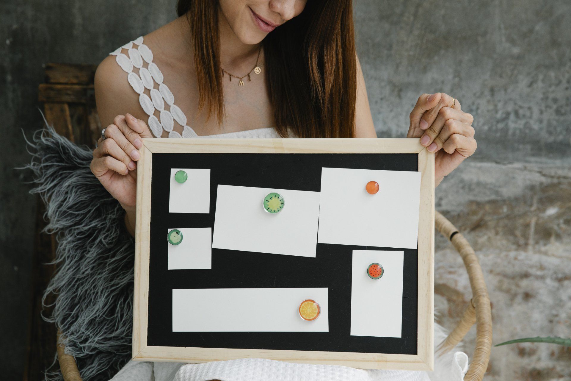Woman holding a black framed bulletin board with white notes pinned with colorful pushpins.