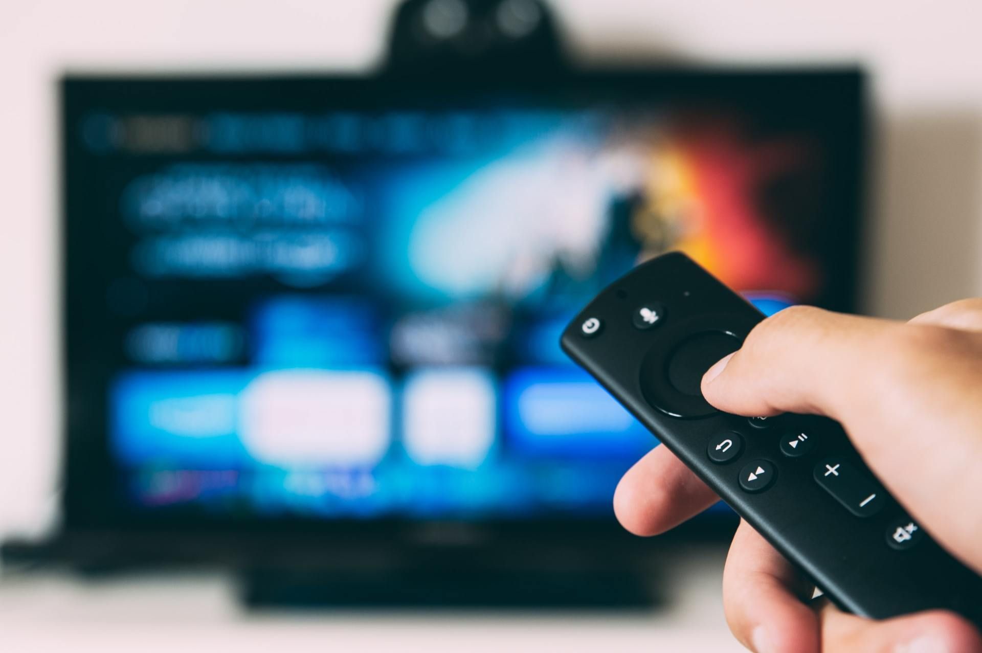 Person holding a black remote, pointing it at a blurred television screen.