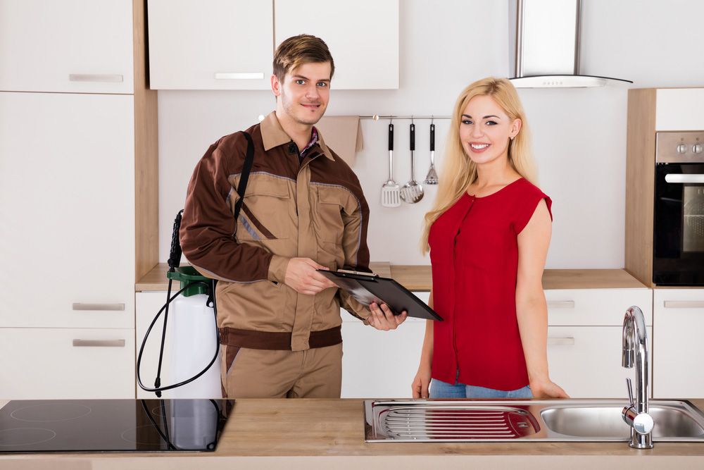 Woman Signing Invoice From Exterminator Worker After Pest Control Worker In House Kitchen — Pest Control Services in Quirindi, NSW