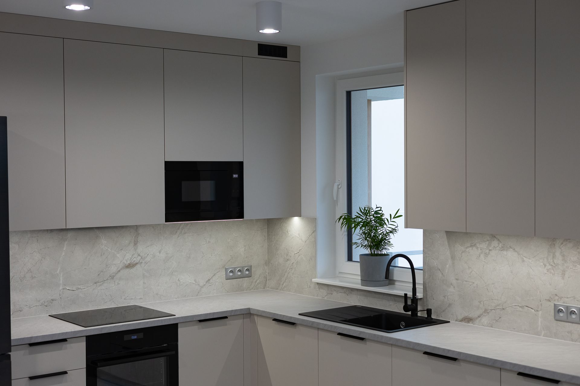 Modern kitchen featuring light beige cabinetry, white marble-patterned backsplash, black appliances, and a window sink. Modern kitchen featuring light beige cabinetry, white marble-patterned backsplash, black appliances, and a window sink.