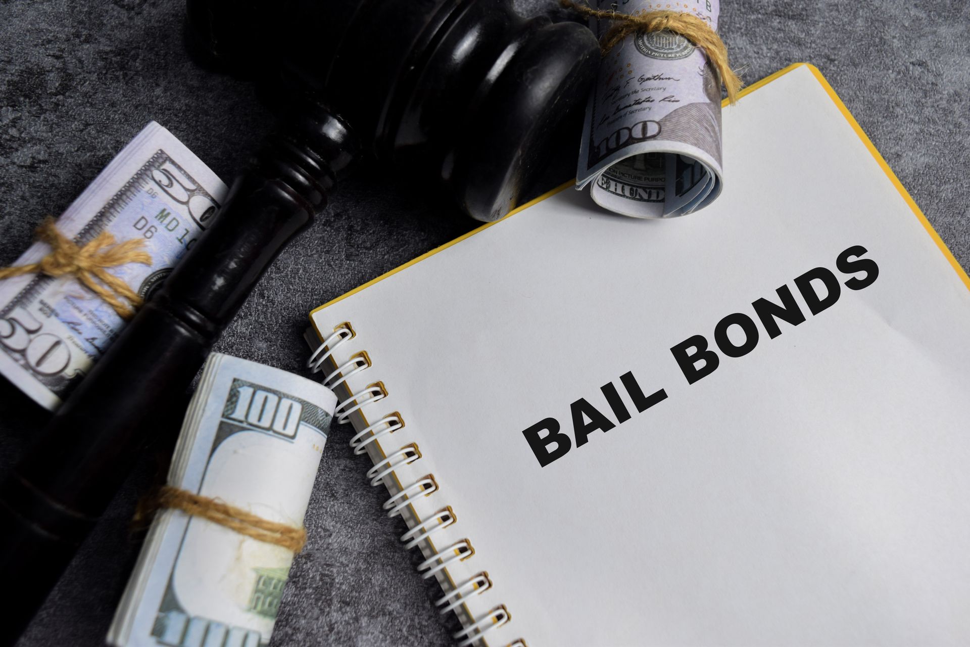 Bail bonds notebook with cash bundles and gavel on dark surface.