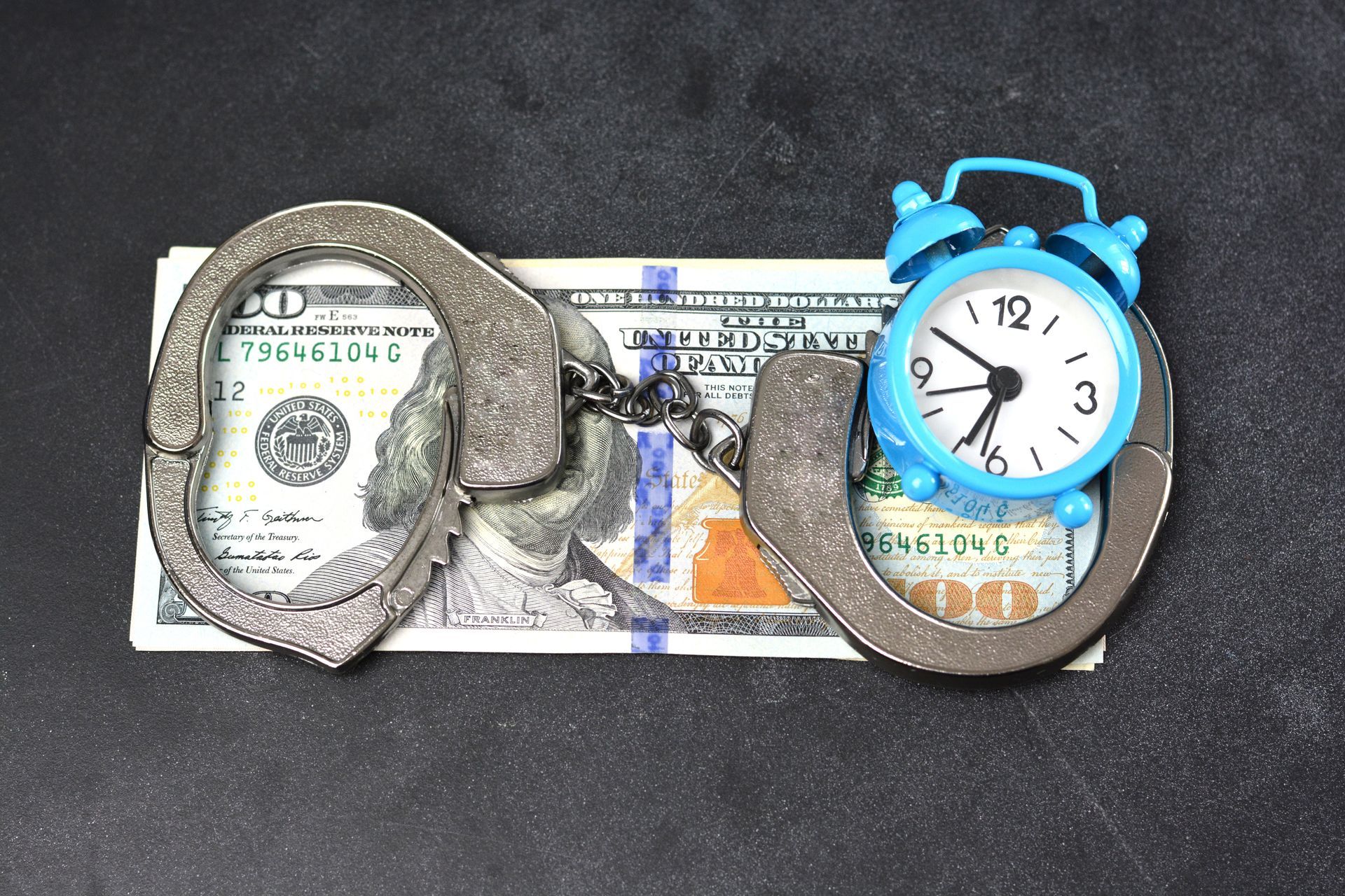 Handcuffs, money, and an alarm clock on a dark background. Handcuffs, money, and an alarm clock on a dark background.