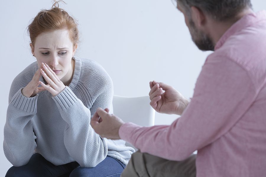 Woman in distressed expression, seated opposite a person, likely in therapy session.