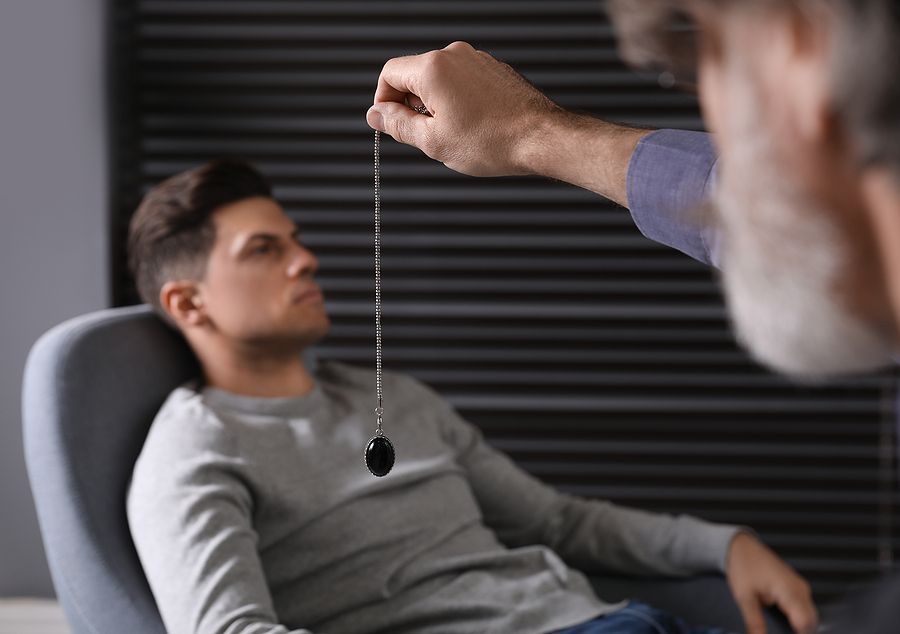 Man in chair being hypnotized by another man holding a pendulum.