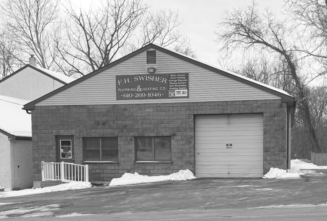 Garage with sign, snow on the ground, trees in the background.