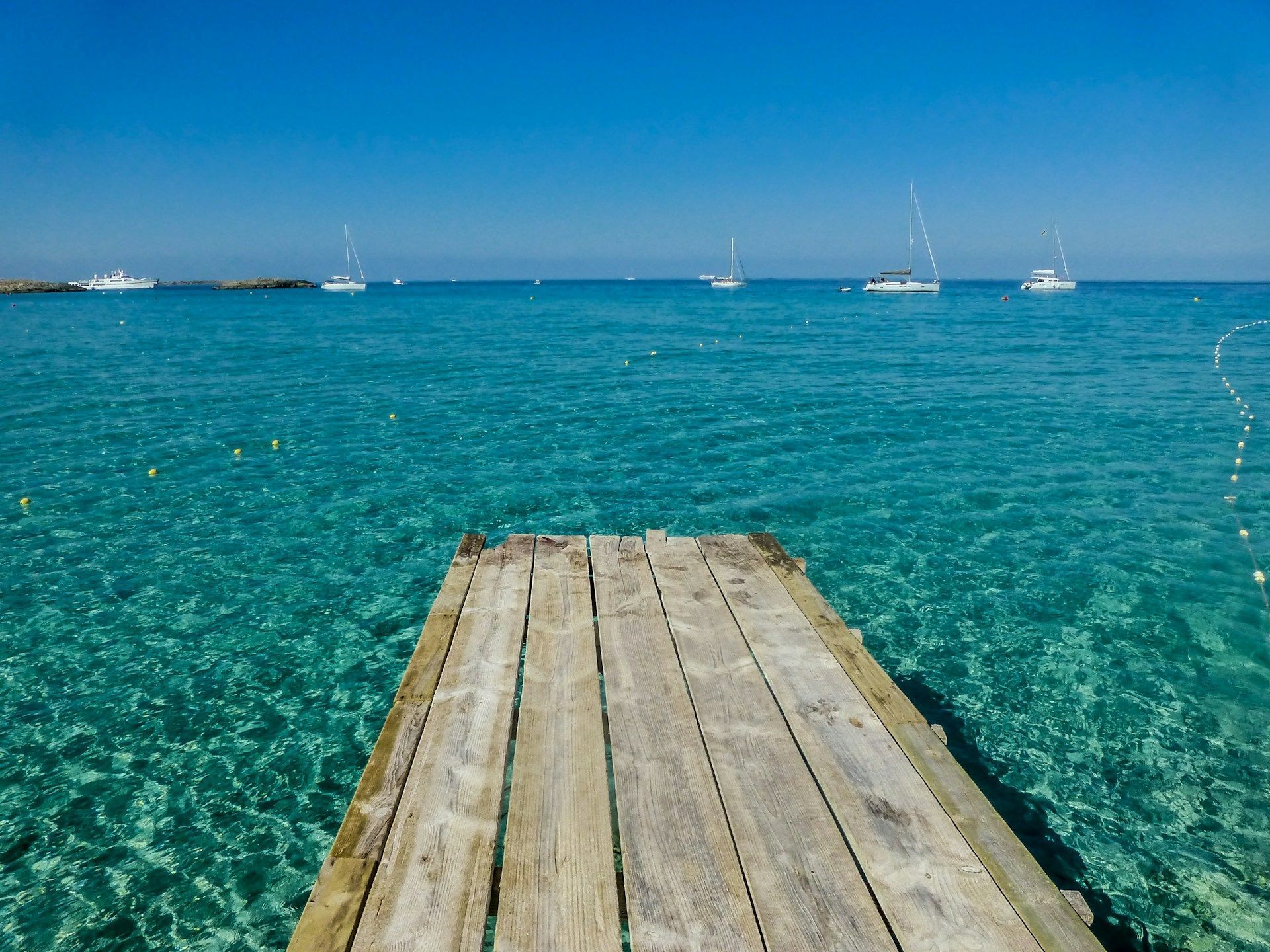 A wooden pier leading into the ocean with boats in the distance.