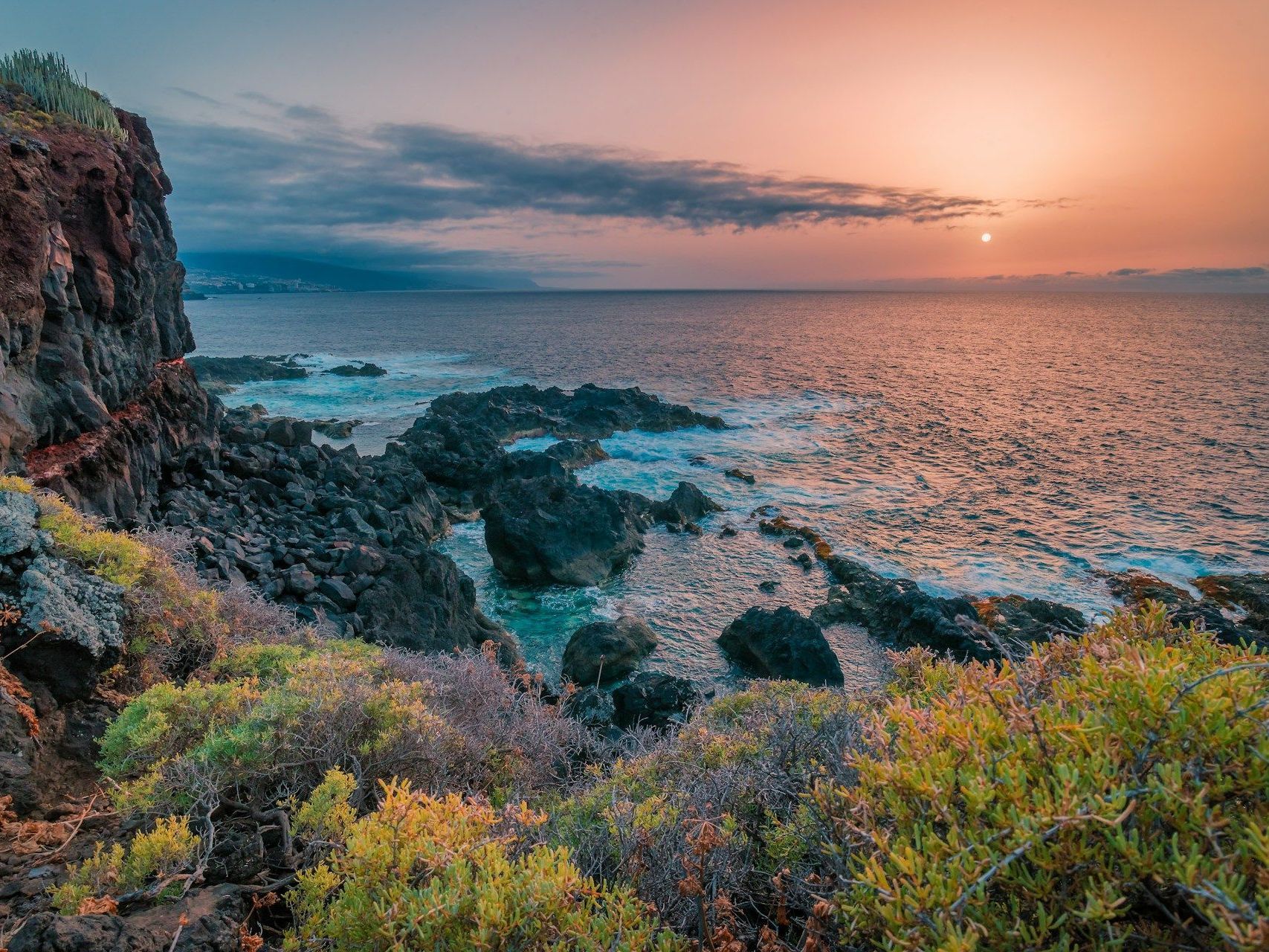 A sunset over the ocean with a rocky shoreline in the foreground.