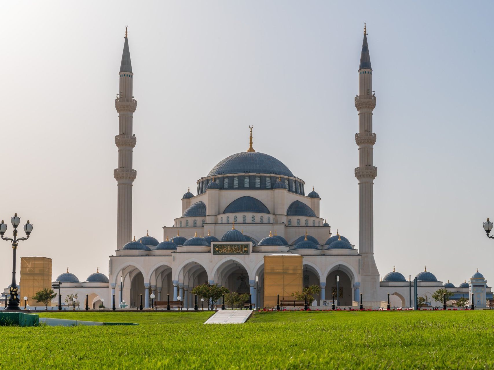 A large white mosque with a blue dome is surrounded by green grass.