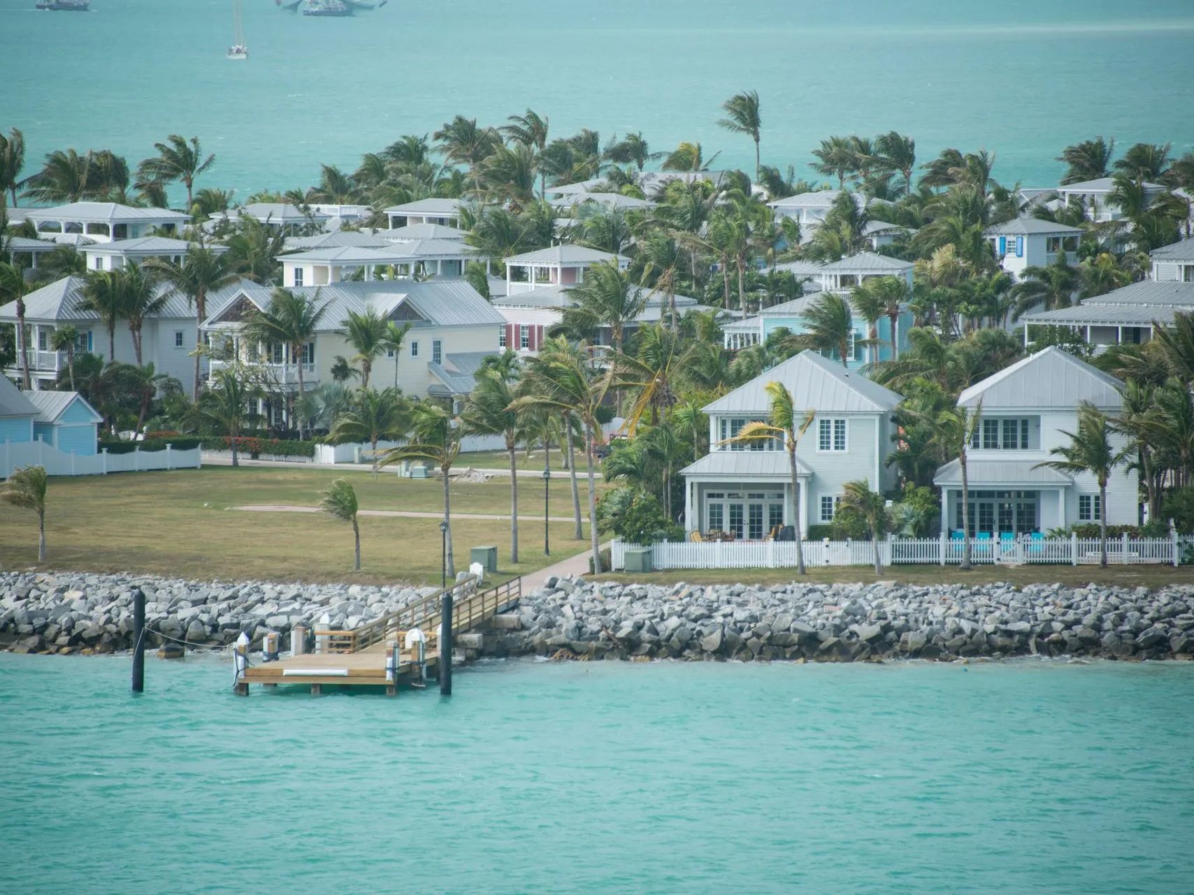 A boat is docked in front of a row of houses on a tropical island.