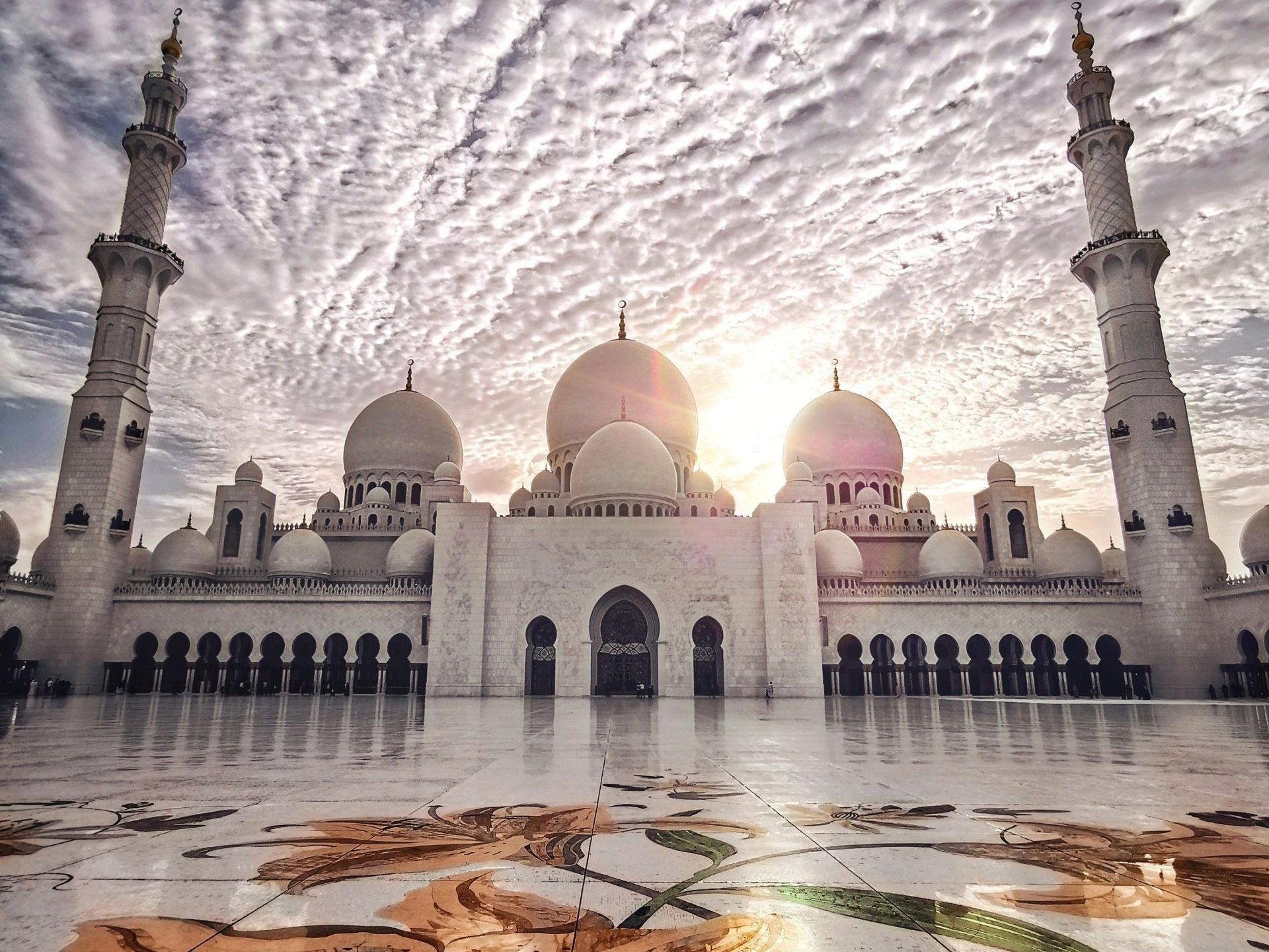 A large white mosque with the sun shining through the clouds