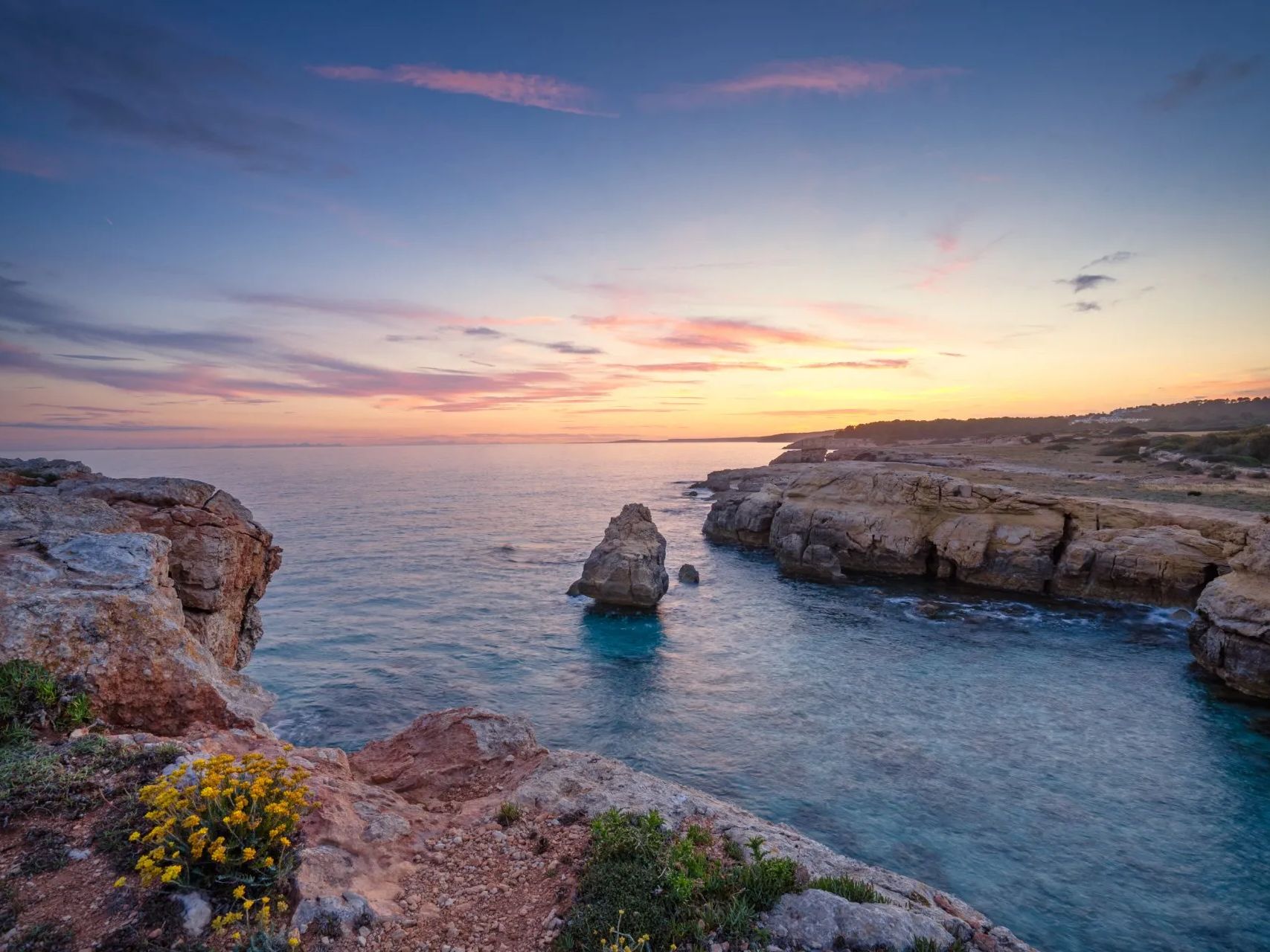 A sunset over a body of water with rocks in the foreground and a cliff in the background.