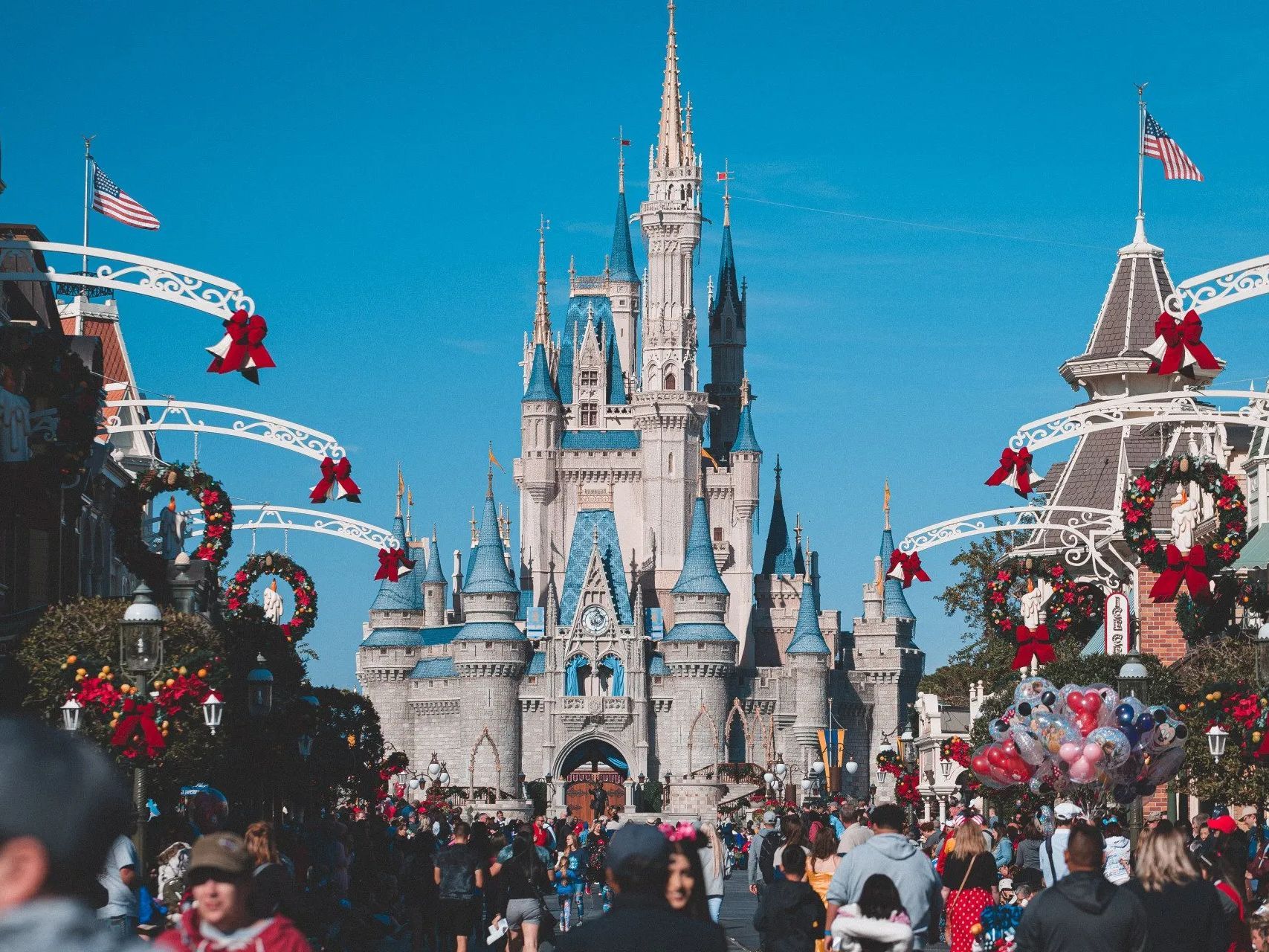 A crowd of people are walking in front of a castle at disney world.