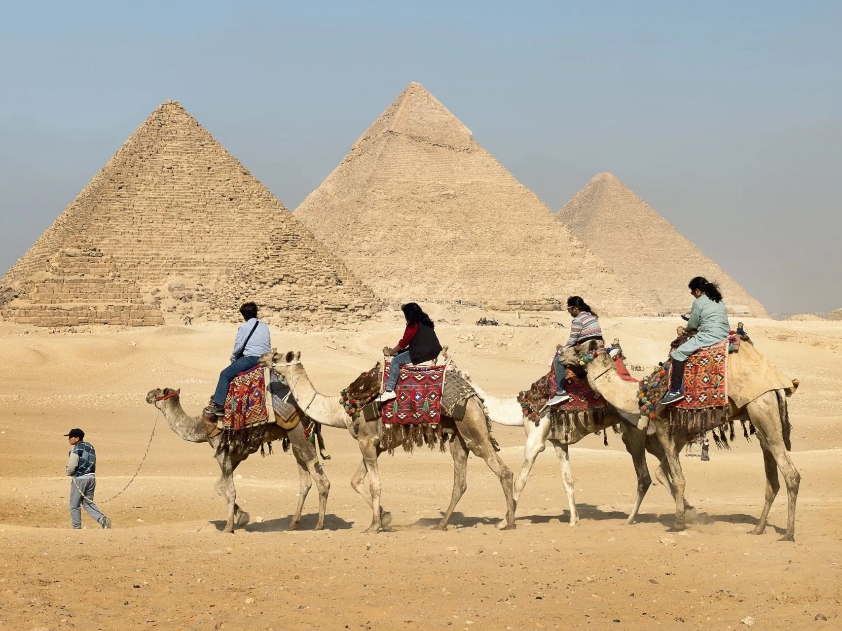 A group of people riding camels in front of pyramids