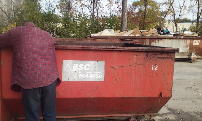 a man is standing next to a red BSC dumpster.