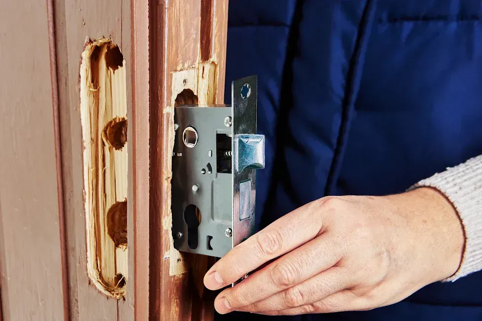 Person installing a silver door lock into a wooden door.