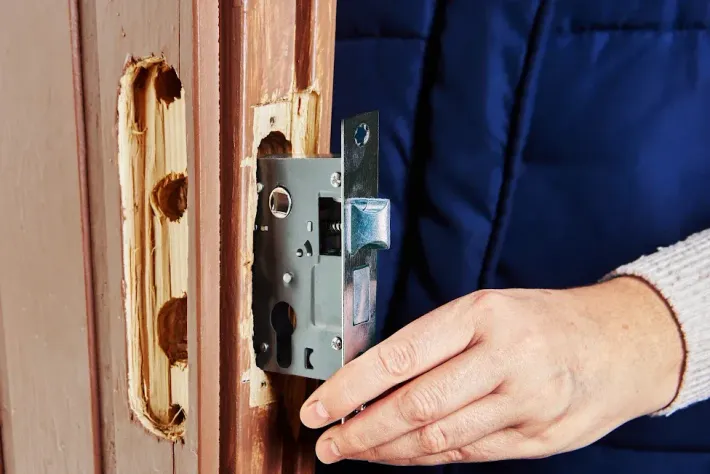 Hand holding a silver door lock next to a door with a carved-out space.