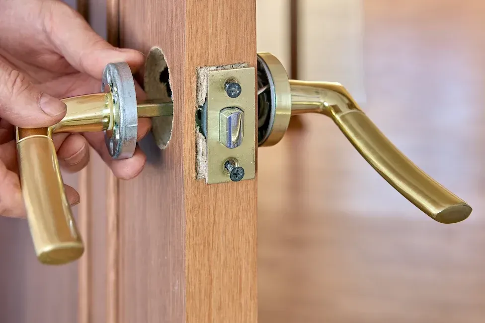 Hand holding a gold door handle, removing it from a wooden door.