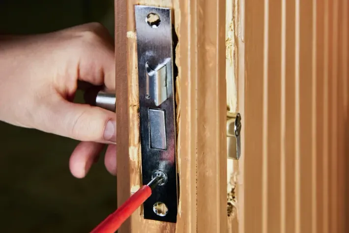 Hand using screwdriver to install door latch on a wooden door.
