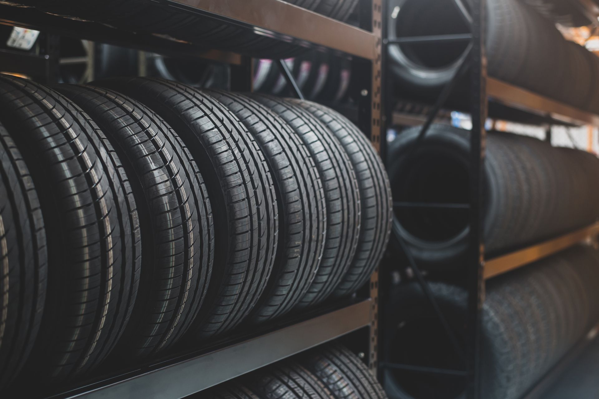 Tires stacked on metal shelves inside a warehouse. Black rubber with tread patterns.