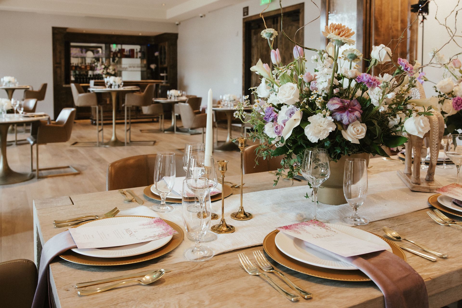 A table set for a wedding reception with plates , candles , and a vase of flowers.