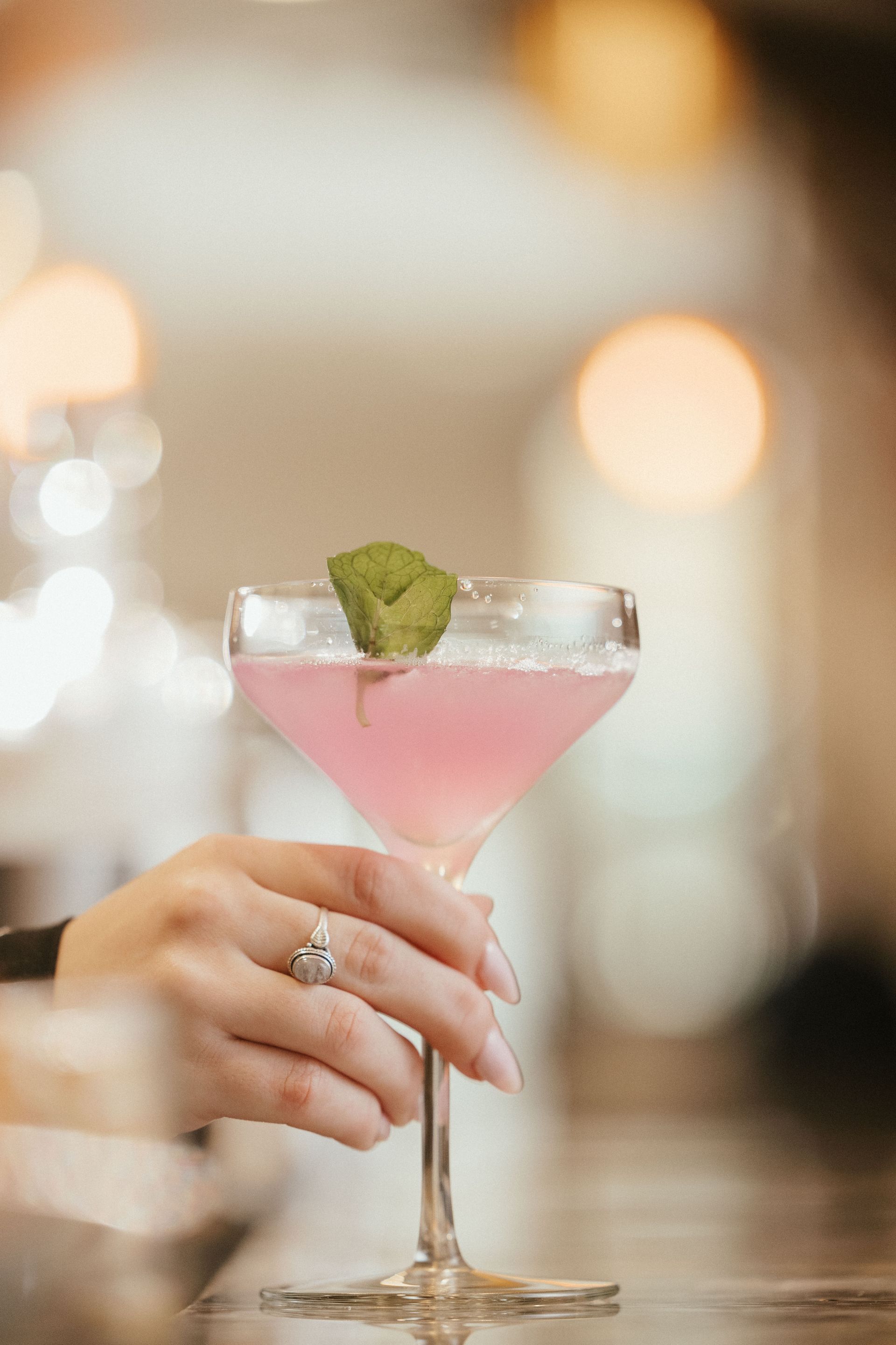 A woman is holding a pink cocktail in a martini glass.