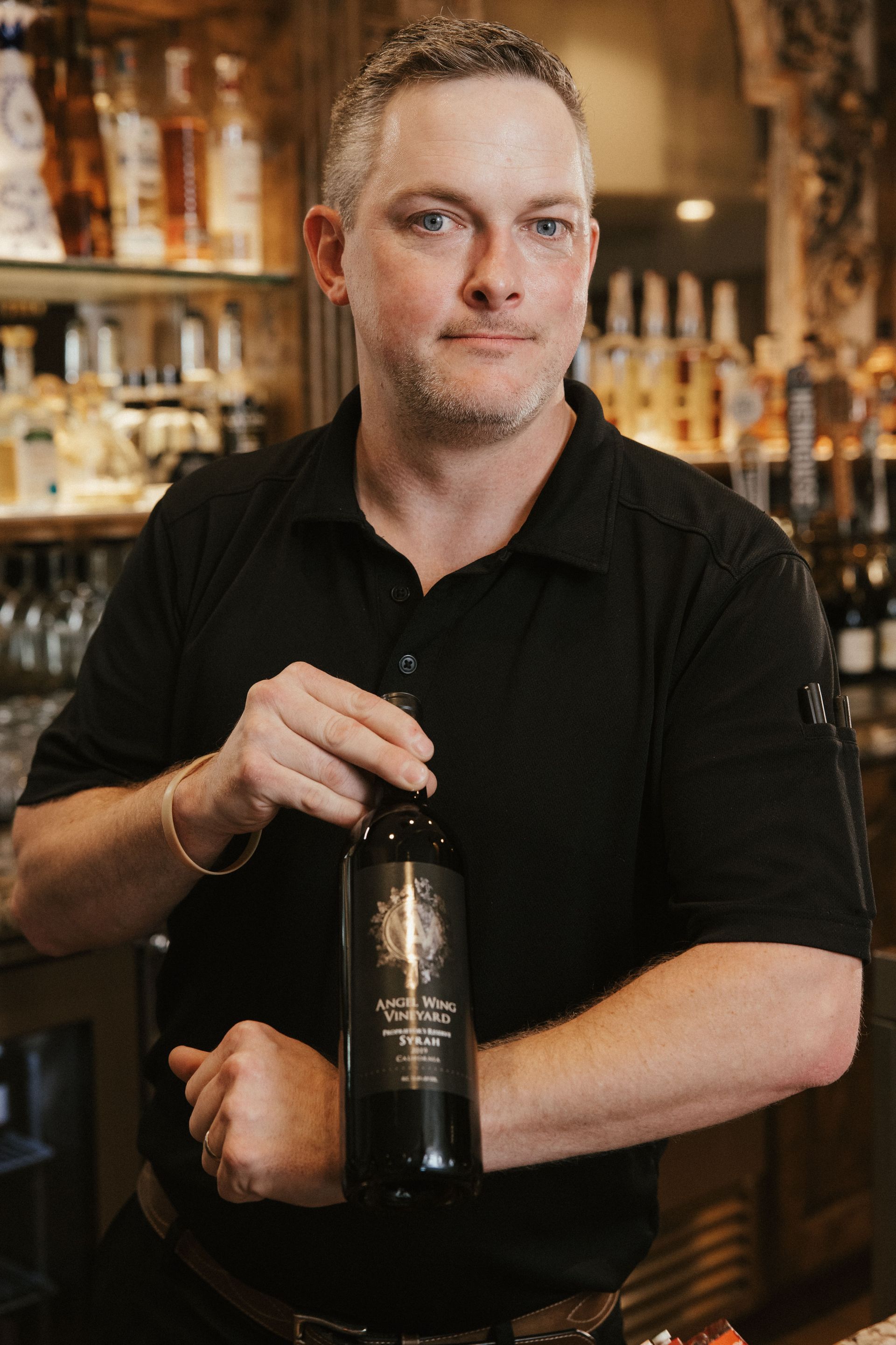 A man in a black shirt is holding a bottle of wine.