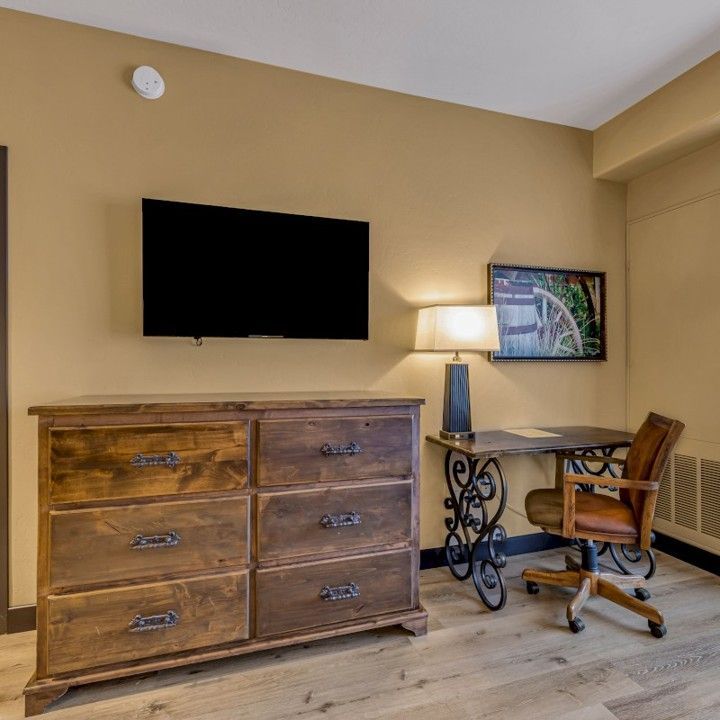 A bedroom with a dresser a desk and a flat screen tv