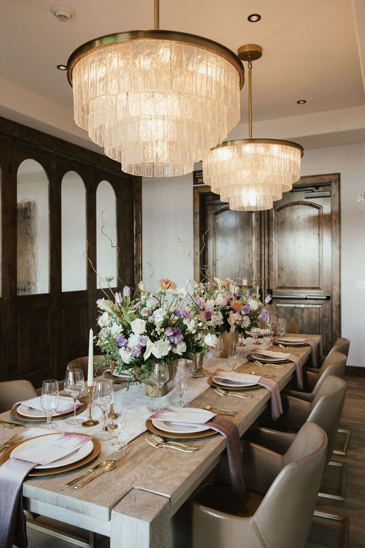 A long dining table with plates , silverware , and flowers on it.