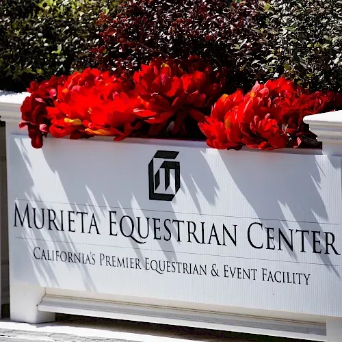 A sign for murieta equestrian center with red flowers