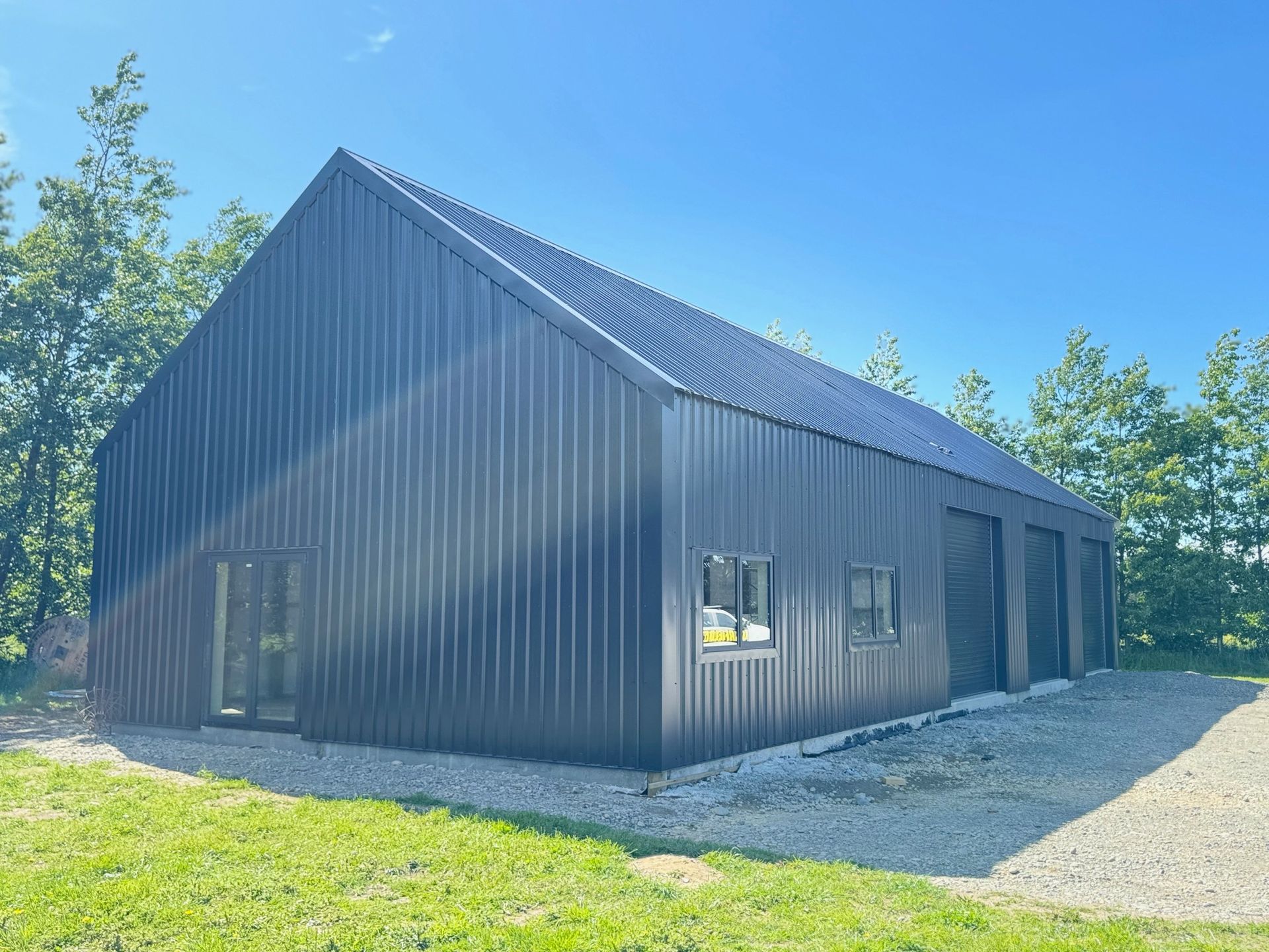 A black metal building with a roof and windows is sitting in the middle of a grassy field.