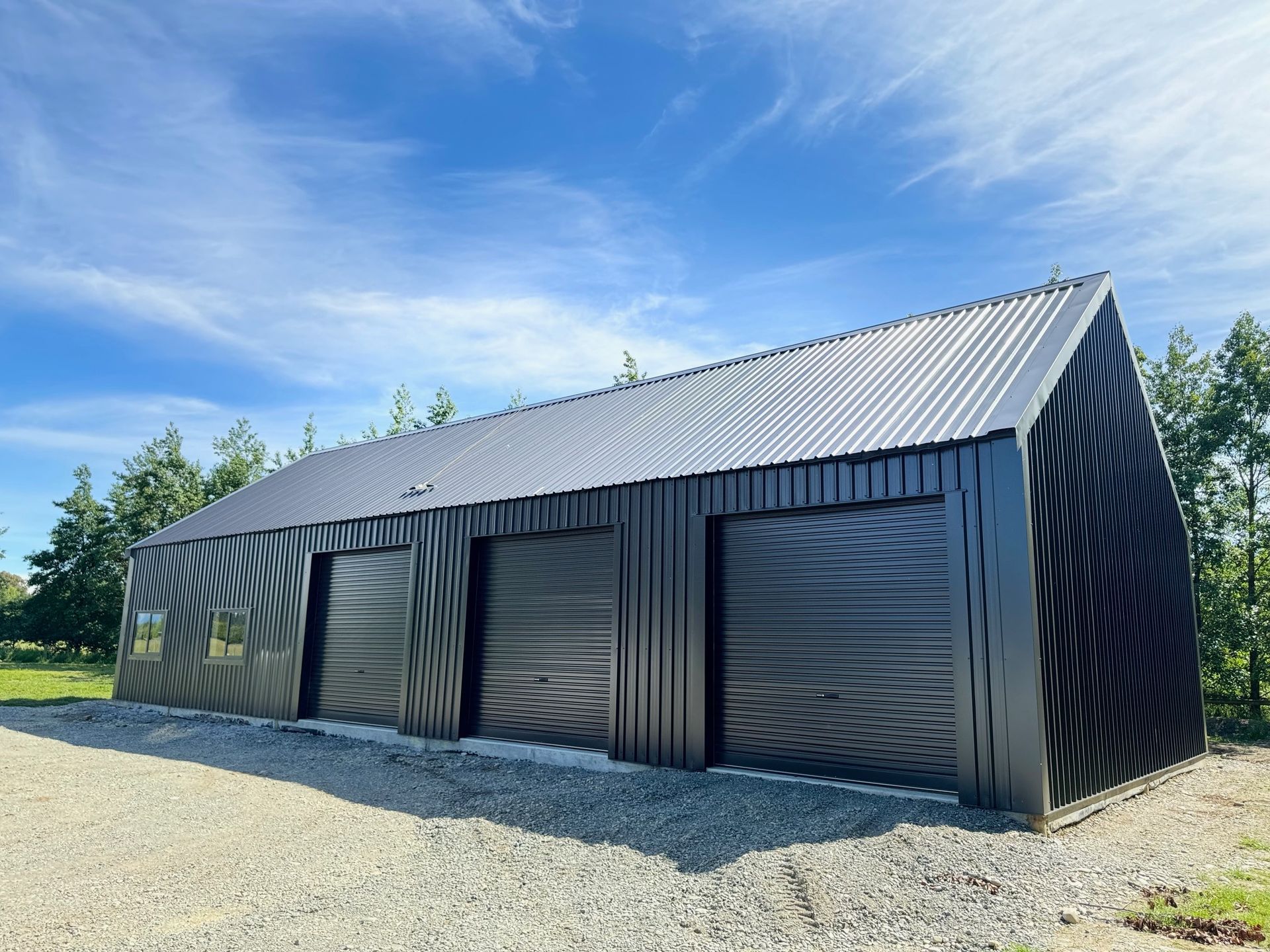 A large black building with three garage doors is sitting on top of a gravel road.