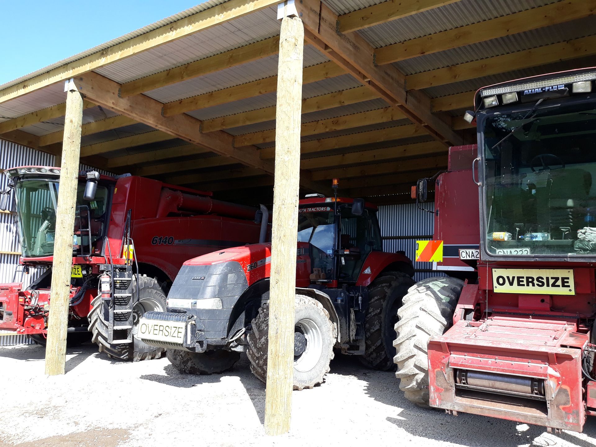 A group of tractors are parked under a wooden structure.