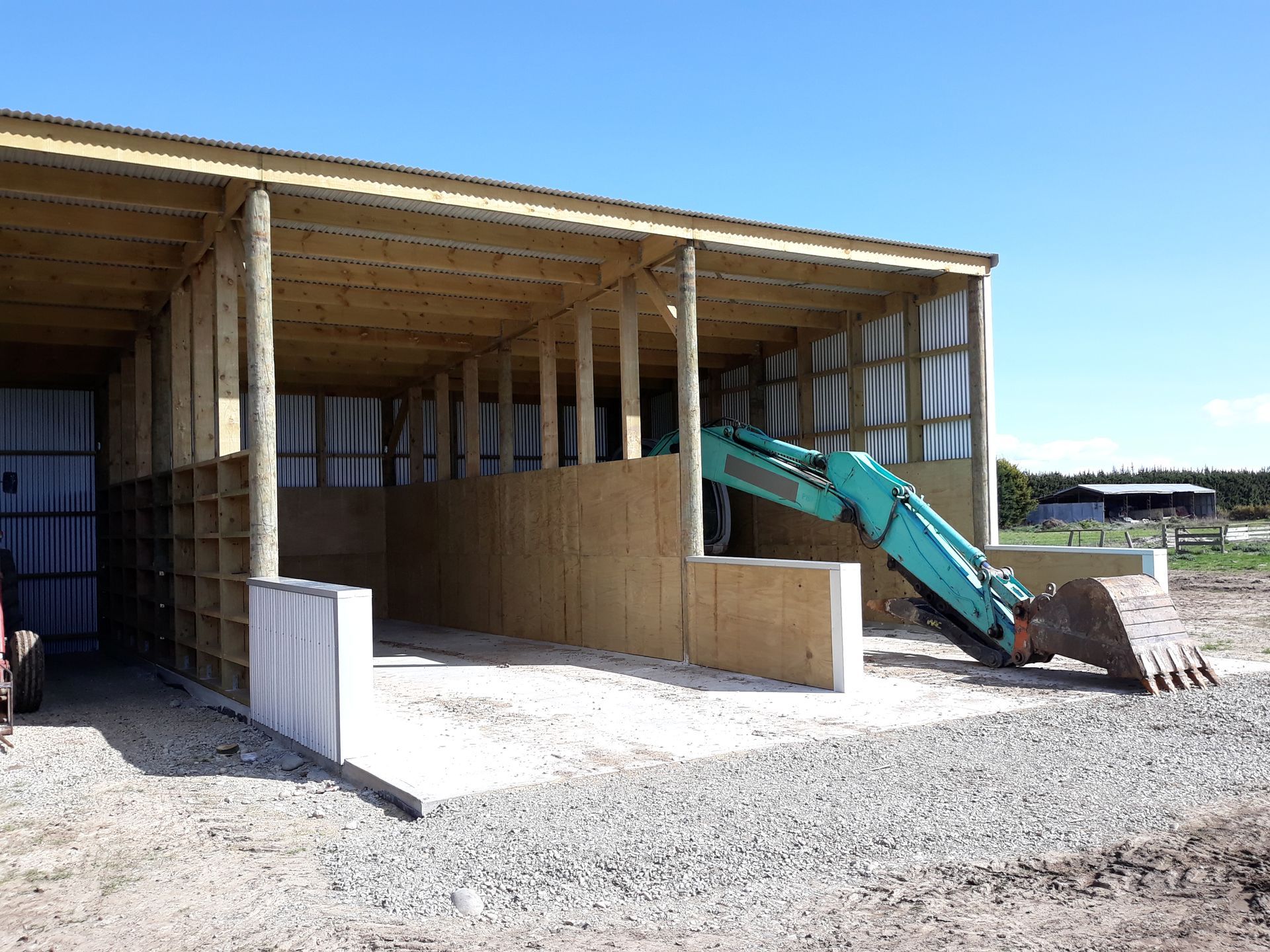A green excavator is parked in front of a wooden building.