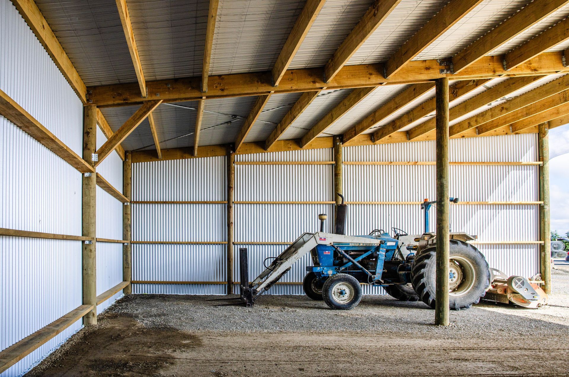 A blue tractor is parked inside of a wooden building.