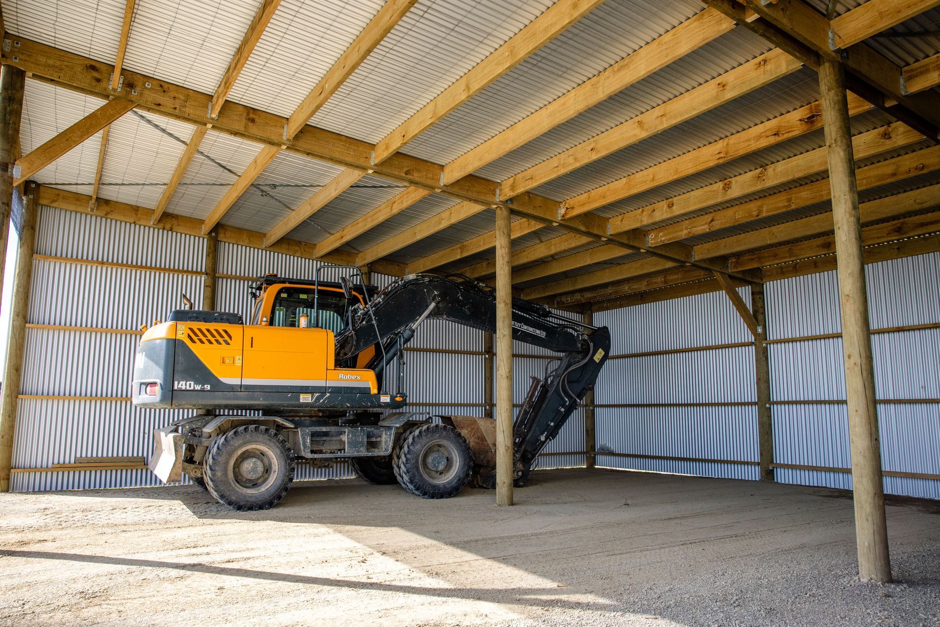 A yellow excavator is parked inside of a wooden building.