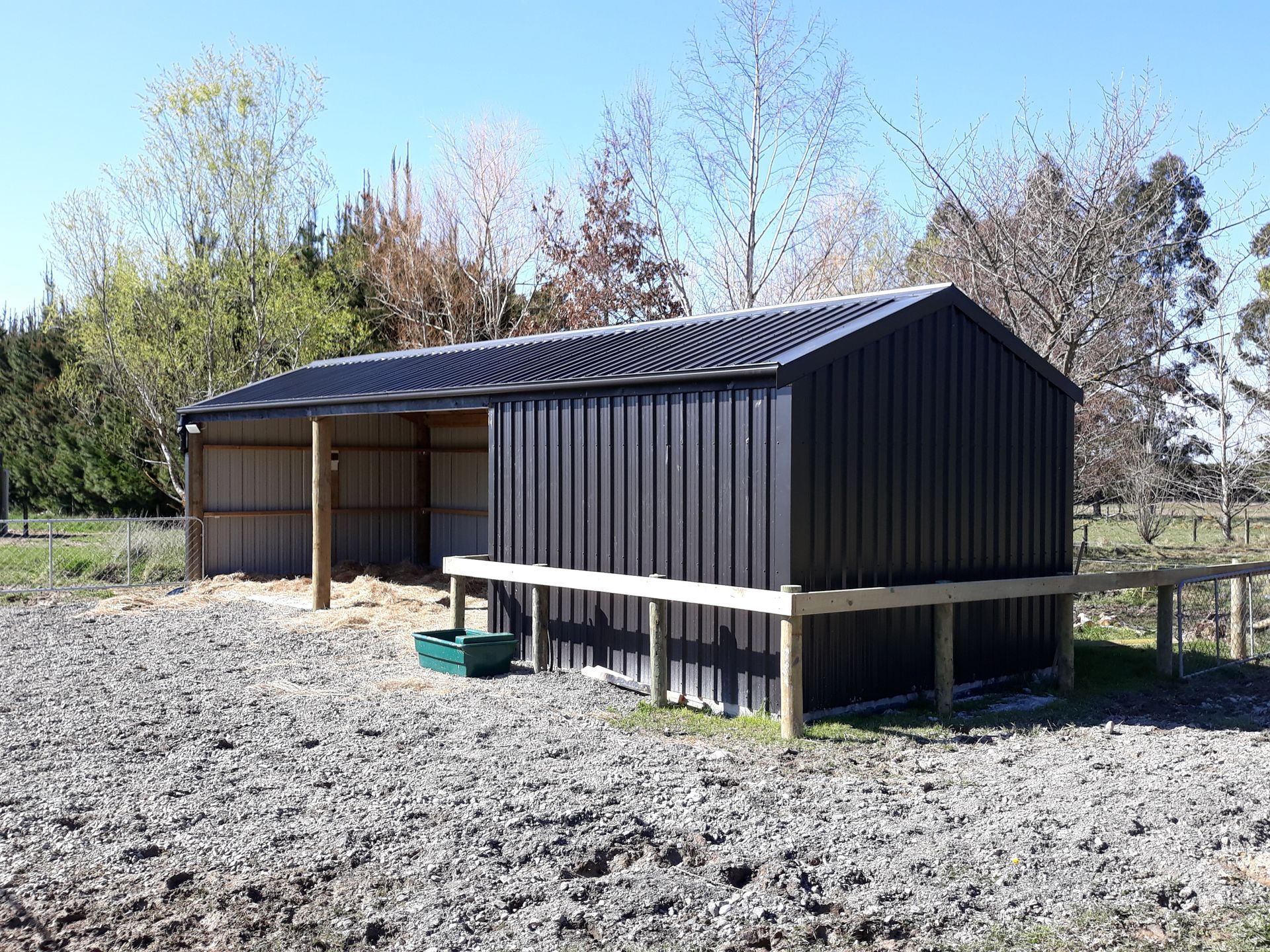A black shed is sitting in the middle of a gravel field.
