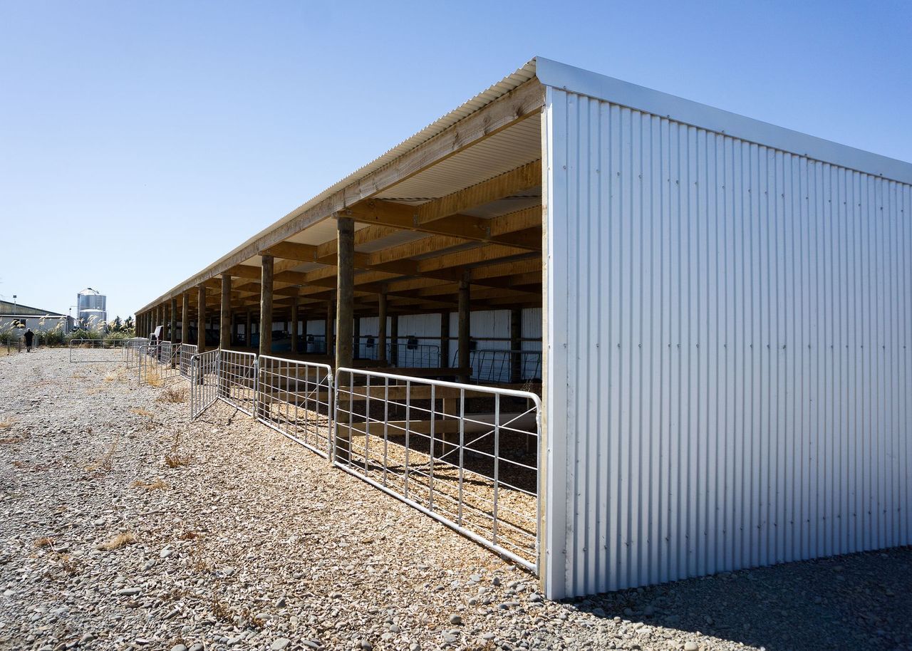 A white building with a wooden roof is surrounded by gravel.