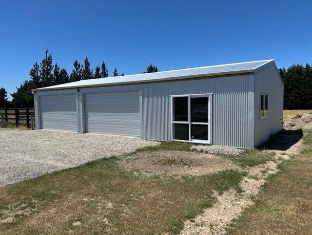 A large gray building with a white roof is sitting in the middle of a grassy field.