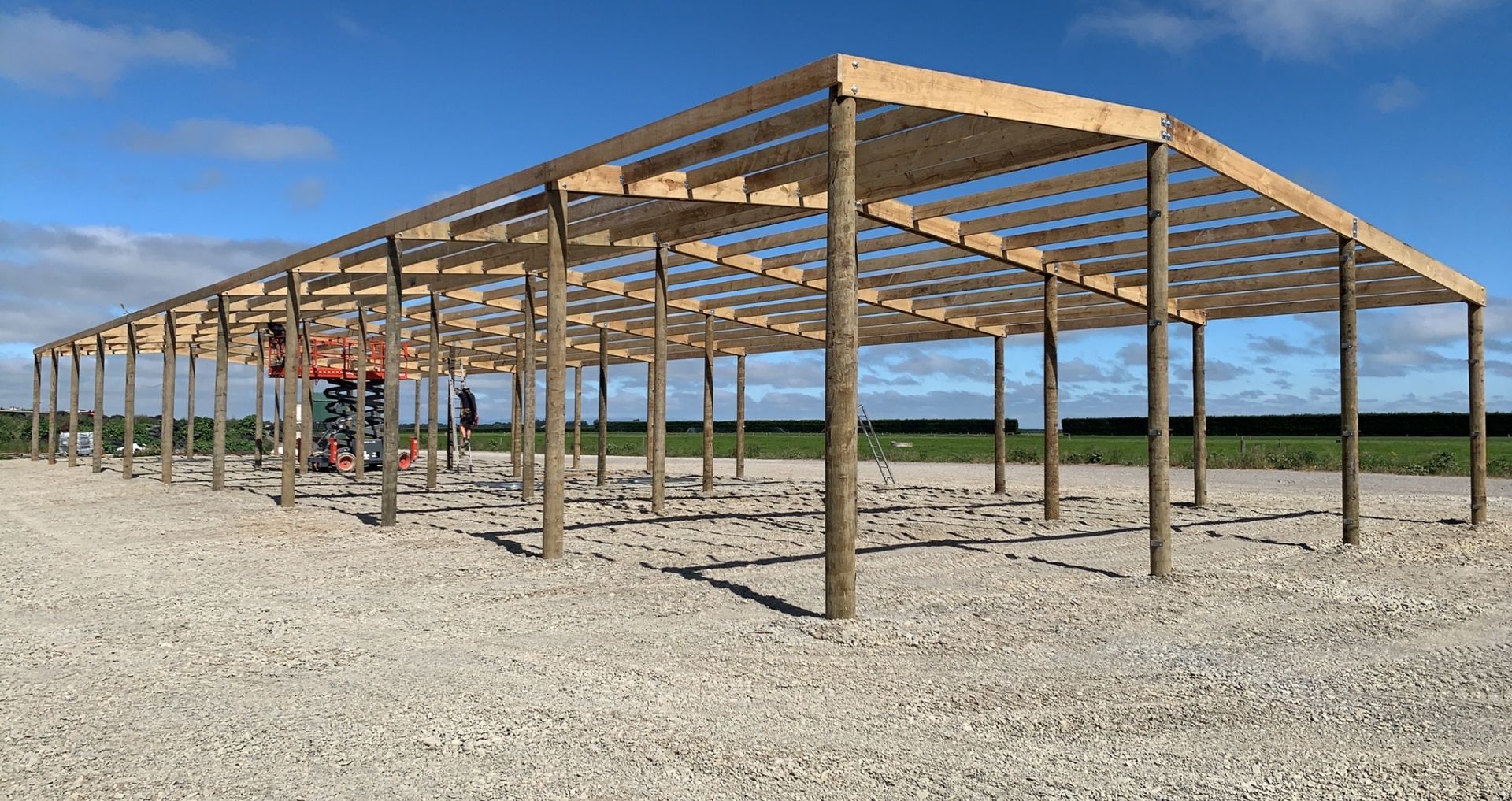 A large wooden structure is being built on a gravel road.