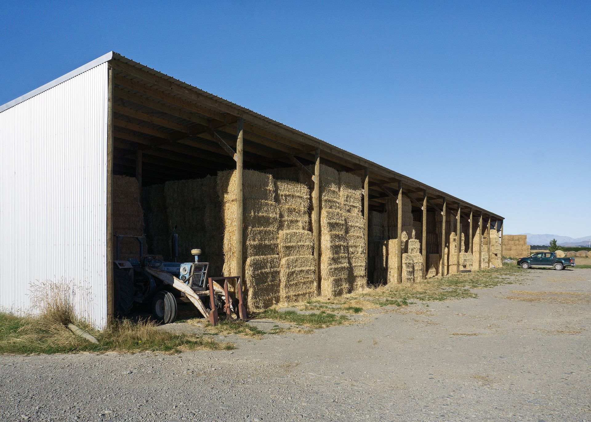 A tractor is parked in front of a barn filled with hay bales.