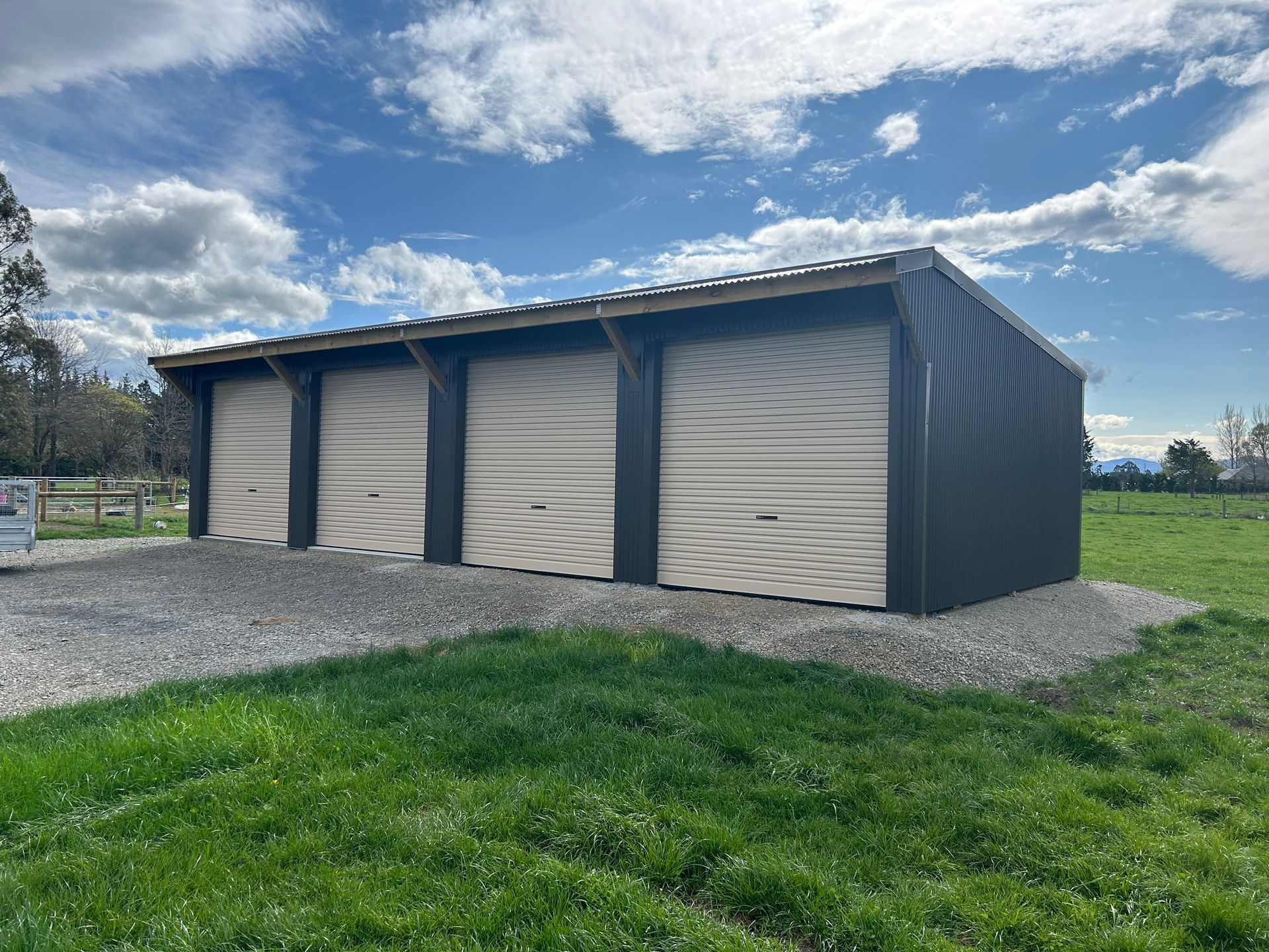 A garage with three garage doors is sitting in the middle of a grassy field.