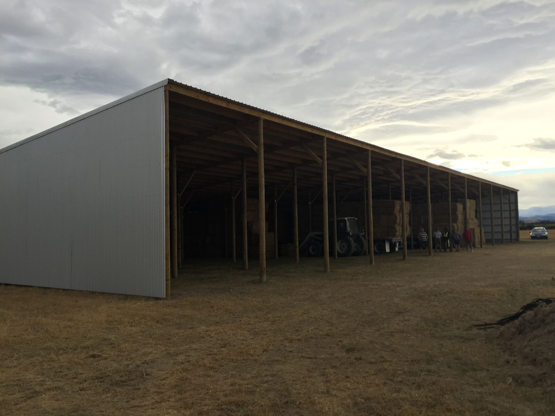 A large metal building with wooden beams is sitting in the middle of a dirt field.