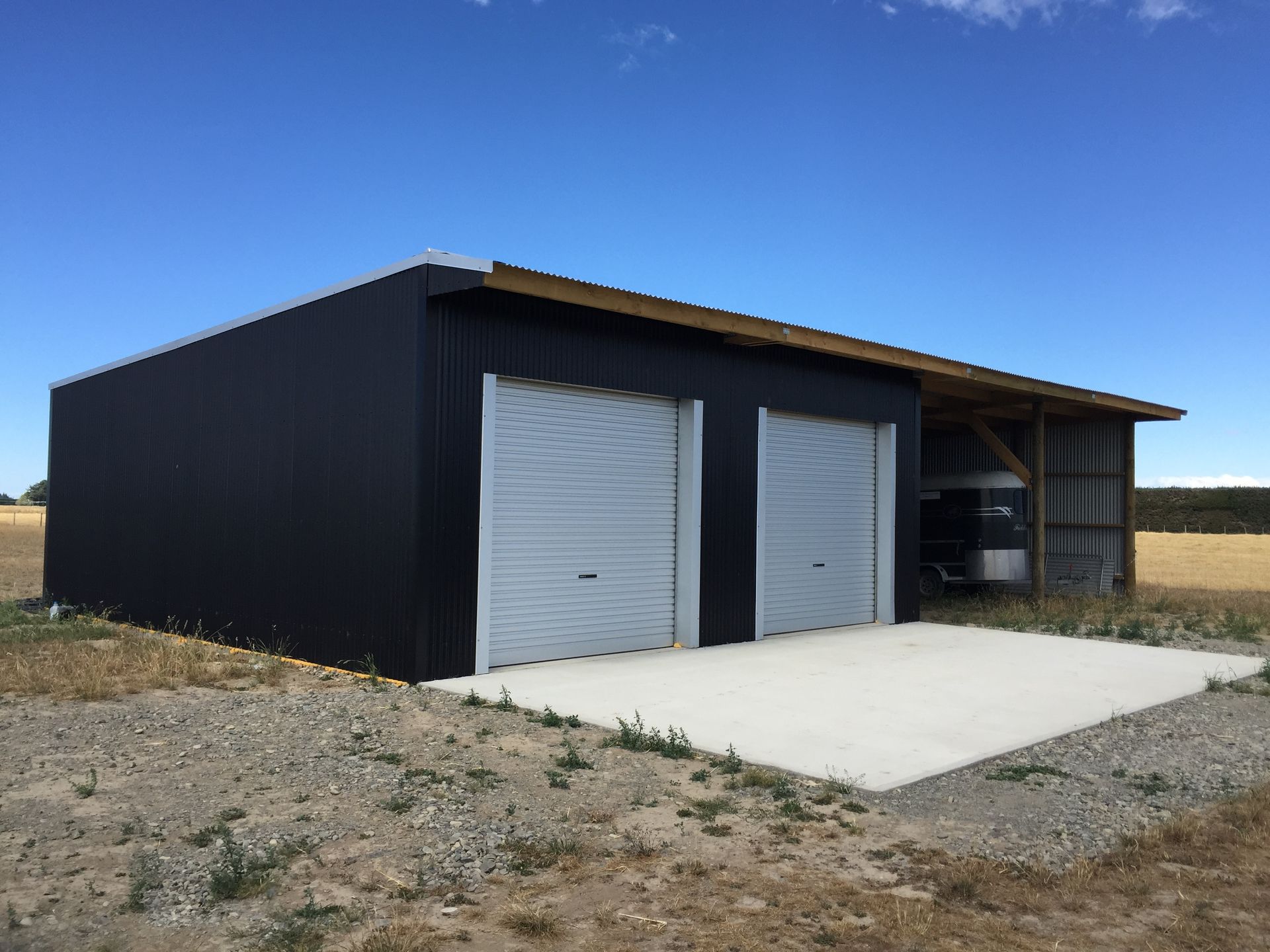 A black building with two garage doors in a field.