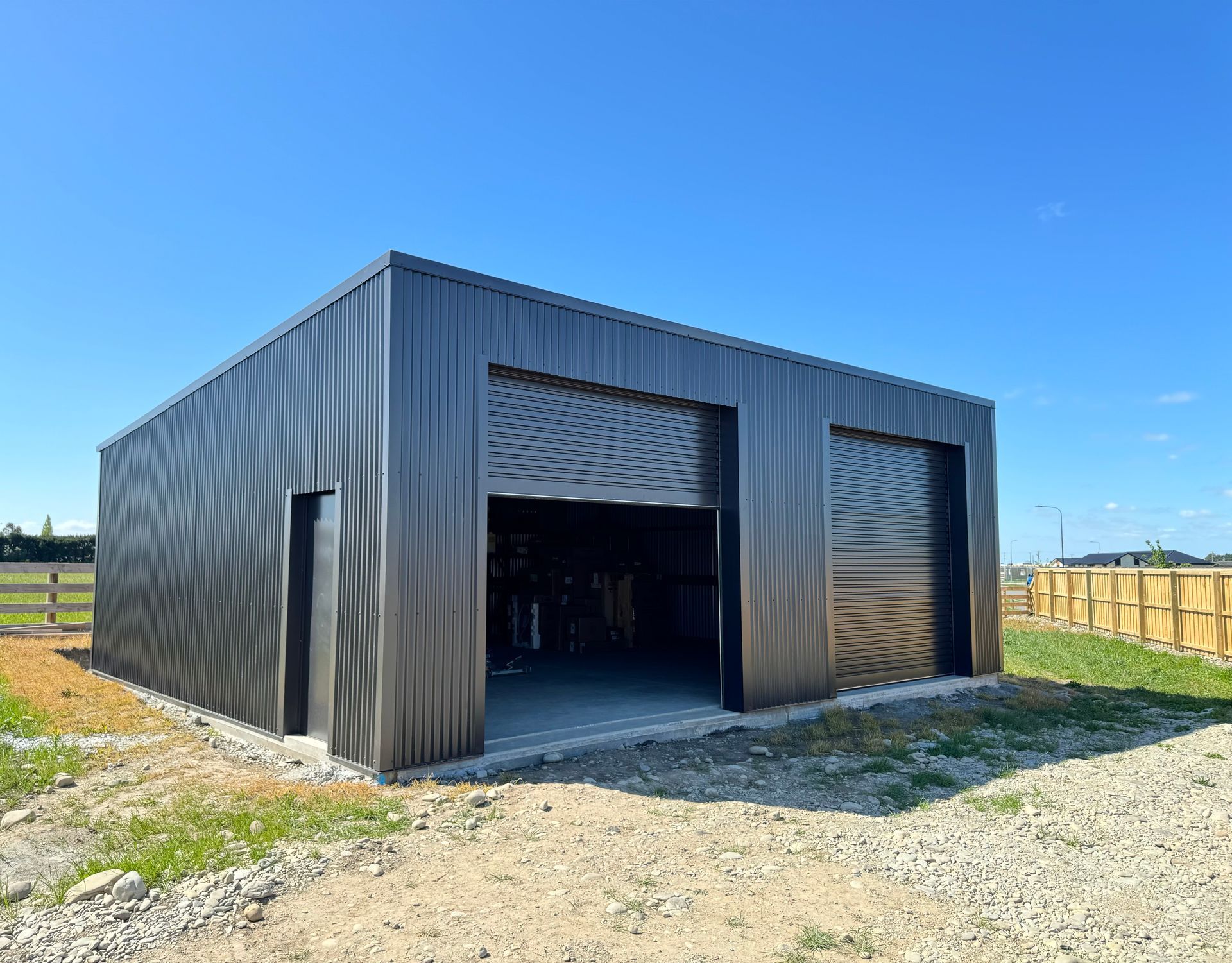 A black metal garage with two garage doors is sitting on top of a dirt field.