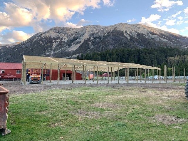 A large wooden building is being built in a field with a mountain in the background.