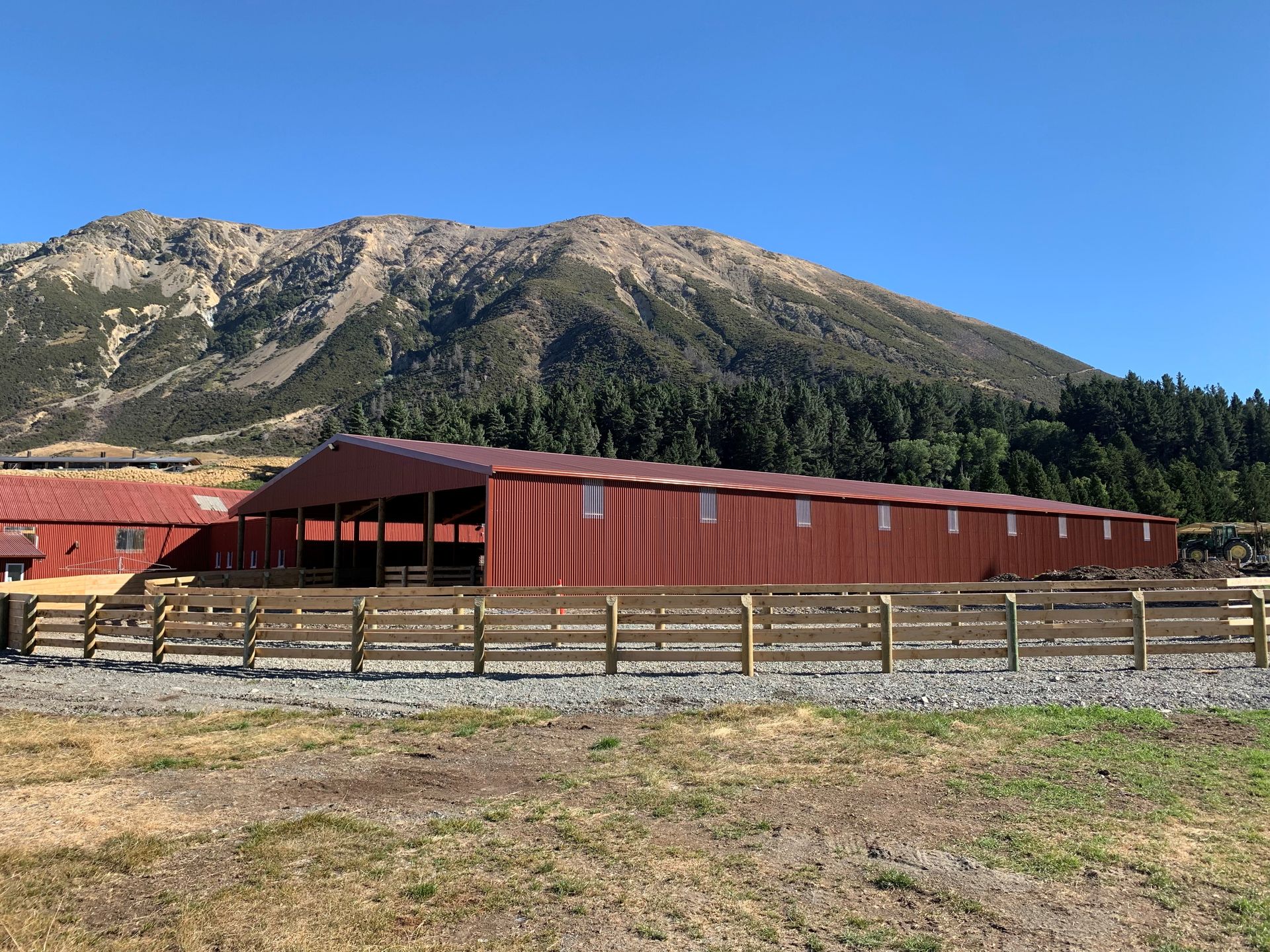 A large red barn with a wooden fence in front of it and a mountain in the background.